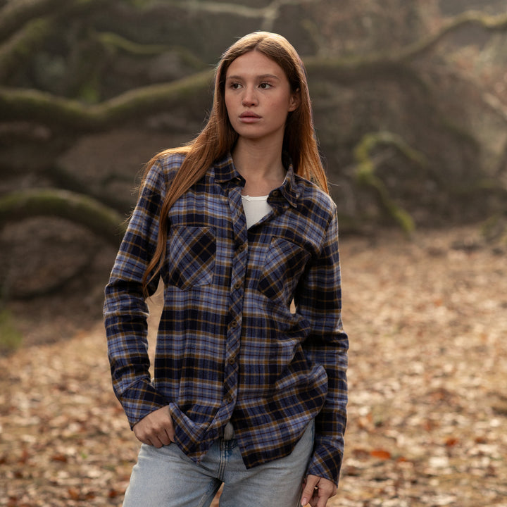 Woman wearing a plaid shirt in a natural setting with trees and ground cover.