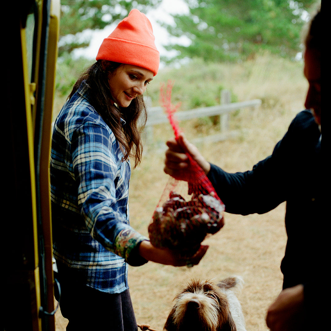 A woman in an orange beanie smiles, wearing Pladra’s Women&