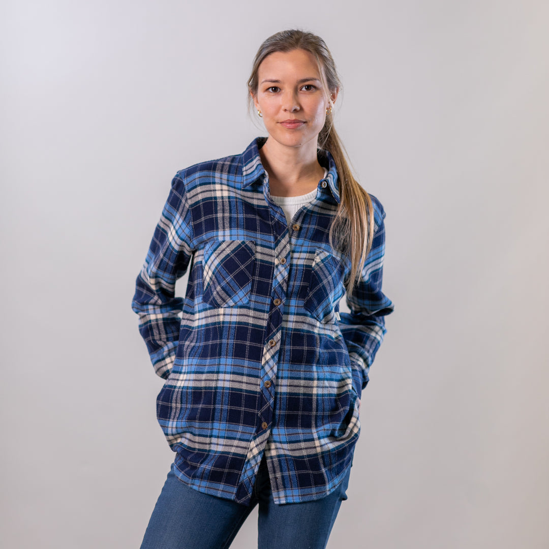 A woman wears the Pladra Women's Every Day Elite Flannel Shirt in Bighorn Blue and jeans, facing the camera.