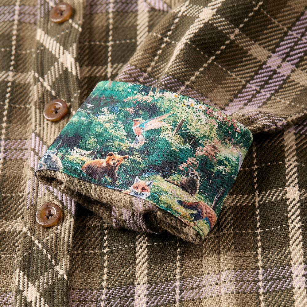Close-up of the Women's Fireside Flannel - Grove Green cuff, turned up to reveal a colorful inner lining featuring red pandas, a fox, a raccoon, greenery, and a bird in flight.