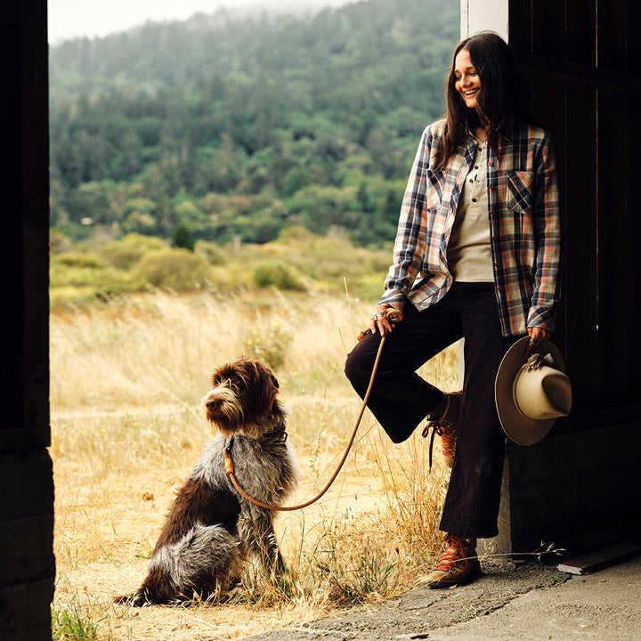 Woman with a dog in a natural setting, leaning against a building.