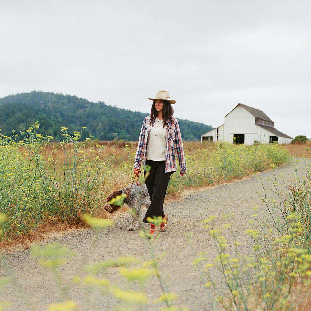 Woman walking a dog on a rural road with a barn in the background