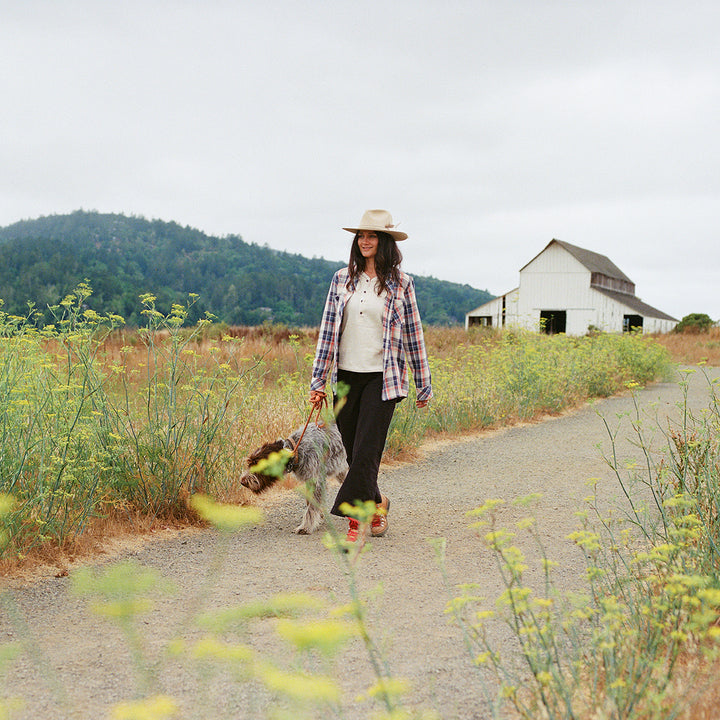 Woman walking a dog on a rural road with a barn in the background