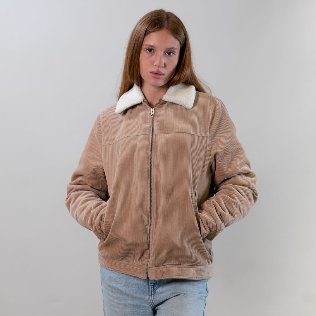 Woman with long hair wears a Pladra Women's Stinson Jacket–Oak Tan and blue jeans, standing against a plain background.
