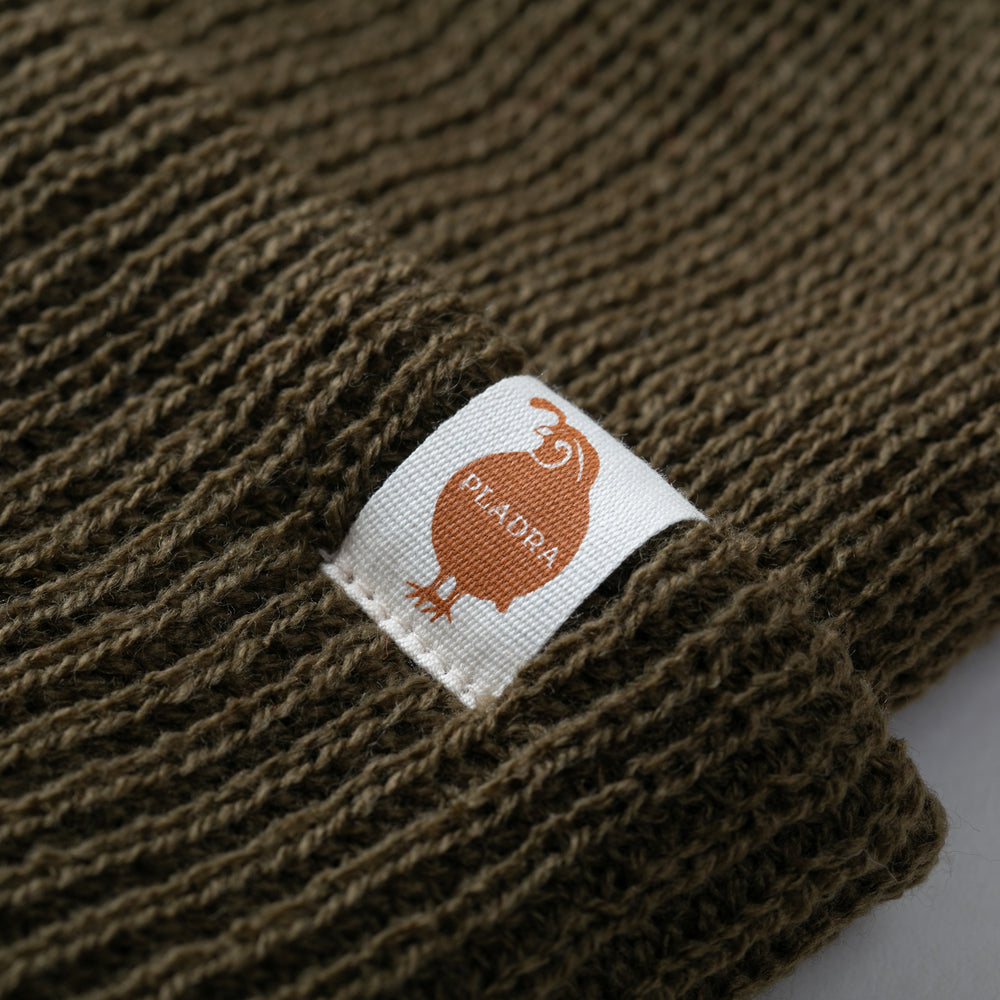 Close-up of an olive green Watch Cap Beanie by Pladra with a white label, made in USA.