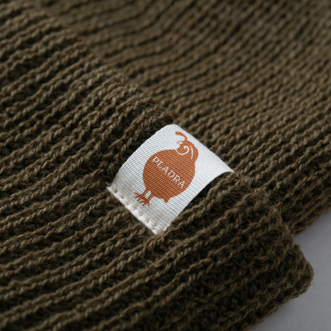 Close-up of an olive green Watch Cap Beanie by Pladra with a white label, made in USA.