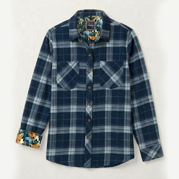 The Women's Fireside Flannel in Laguna Blue is a heavyweight, long-sleeve plaid shirt with two chest pockets and a floral inner collar and cuffs, shown on a simple light background.
