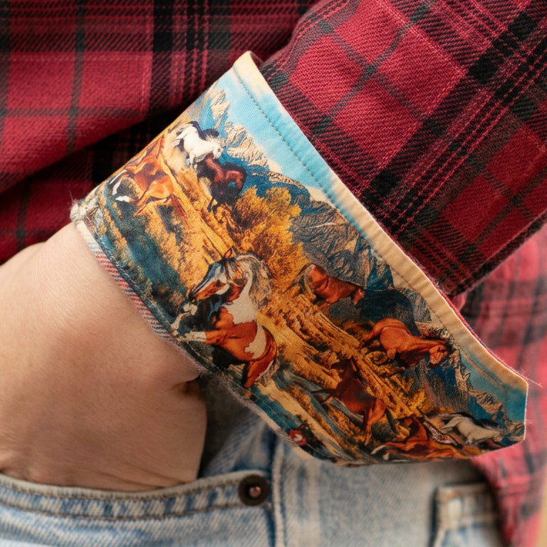 A hand in a jean pocket; cuff of Pladra Women's Every Day Flannel Shirt—Rogue Red, lined with horse print.