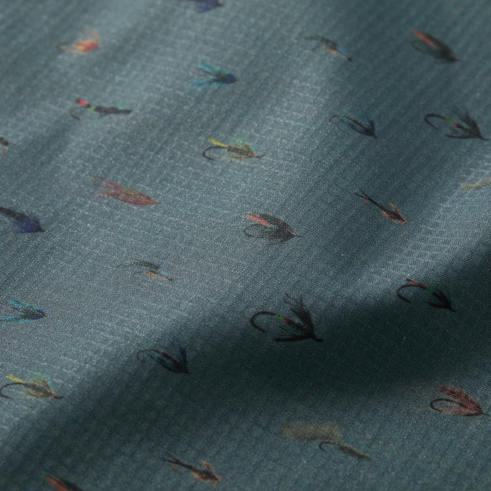 The Men's Yuba Fishing Shirt - Flies Print features quick-drying, UPF 50+ fabric with a subtle grid texture and a repeating pattern of small, colorful fishing flies on a muted blue-green background.