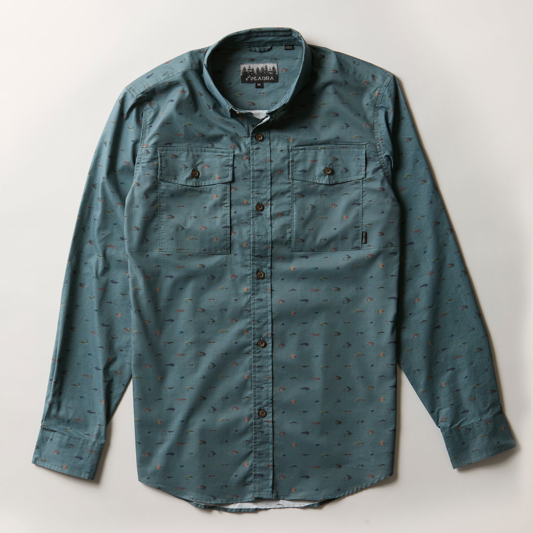 The Men's Yuba Fishing Shirt - Flies Print is a teal long-sleeve button-up made from durable ripstop fabric, featuring two chest pockets and a subtle small flies print, shown laid flat on a white background.