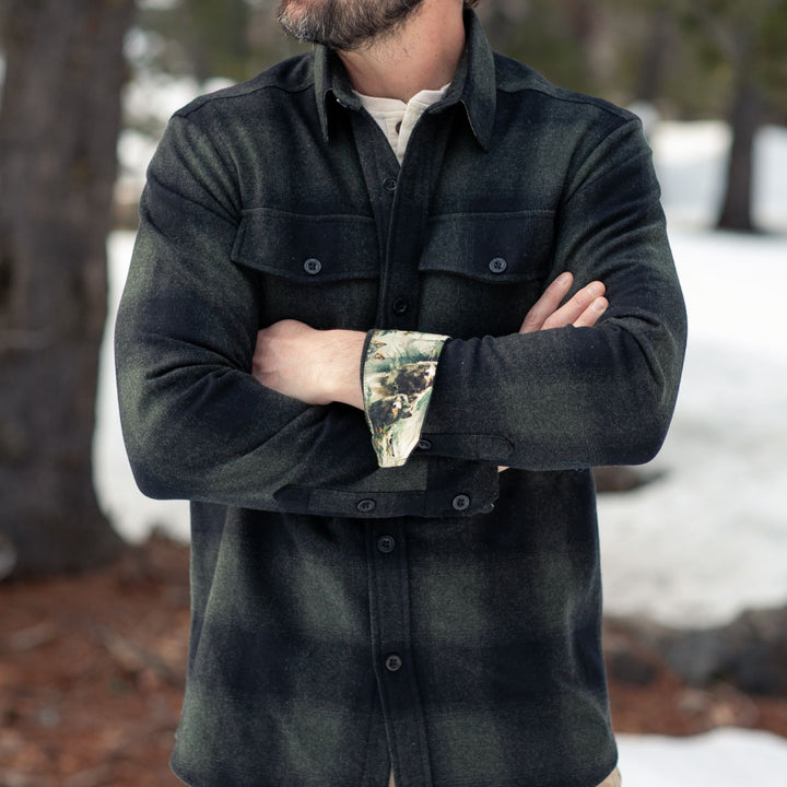 A man stands outdoors in snow, arms crossed, wearing the Men&