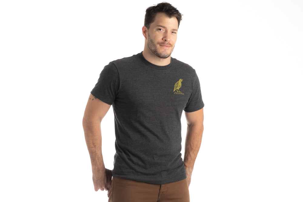 Man with short dark hair wears Pladra Men's Quail Tee in Charcoal Grey Heather, standing against a white background, smiling.