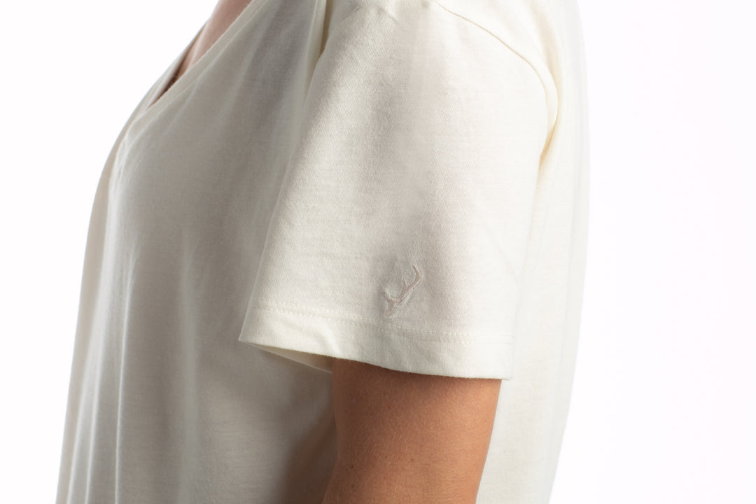 Model in Pladra Women’s V-Neck Tri-Blend Tee—Marshmallow White Heather, side view, logo on sleeve.