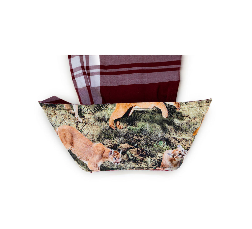 A fabric bowl cozy featuring a mountain lion and grassy landscape print, with textures inspired by the Women's Breeze Shirt in Merlot Red, and holding a maroon and white plaid cloth.