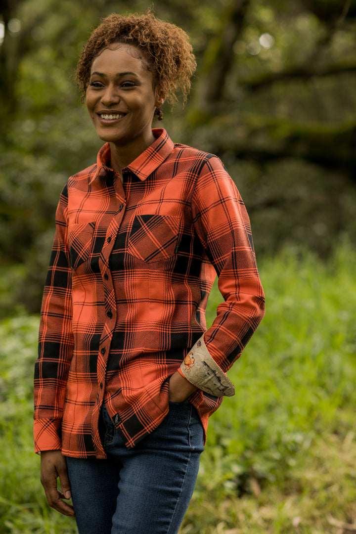 A smiling woman with curly hair stands outdoors, wearing the Women&