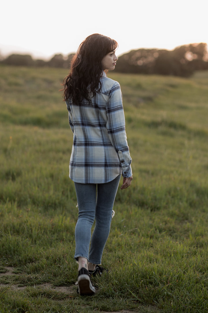 Woman with long dark hair walks in a grassy field at sunset, wearing a Pladra Women&