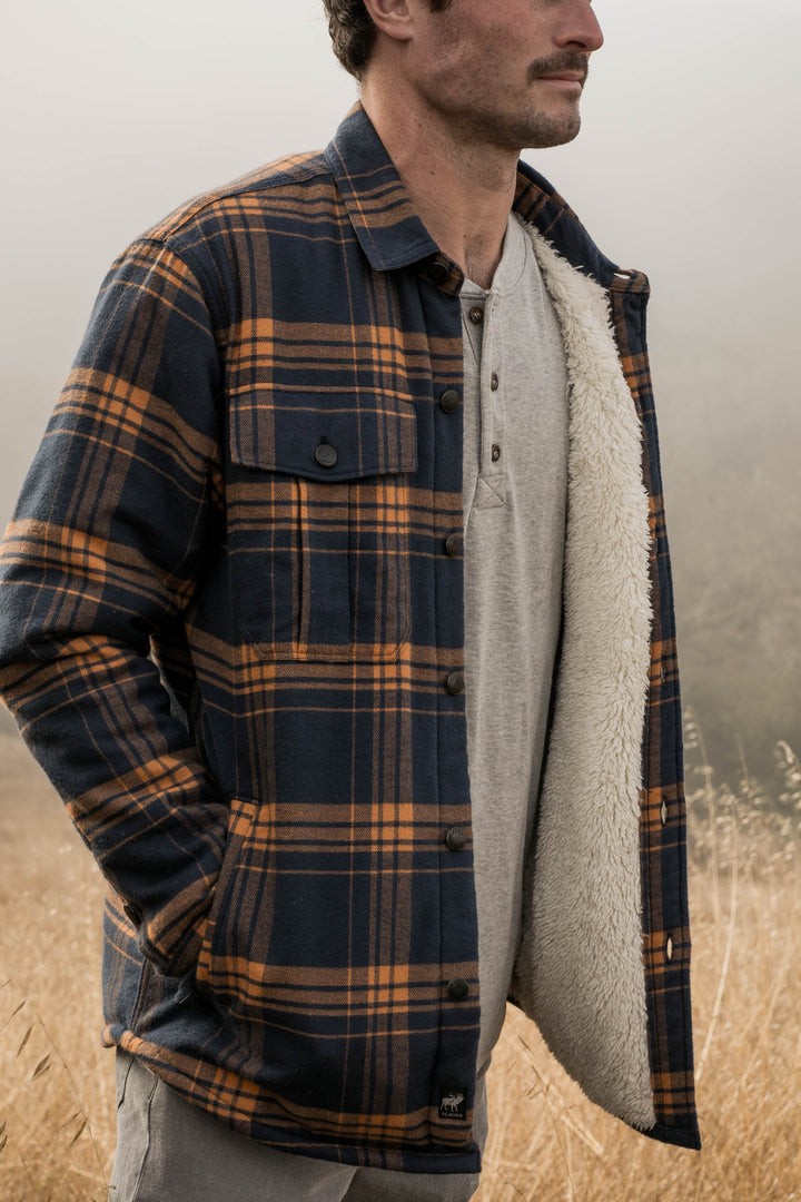 A man stands in a foggy, dry grass field with hands in his pockets, wearing the Men&