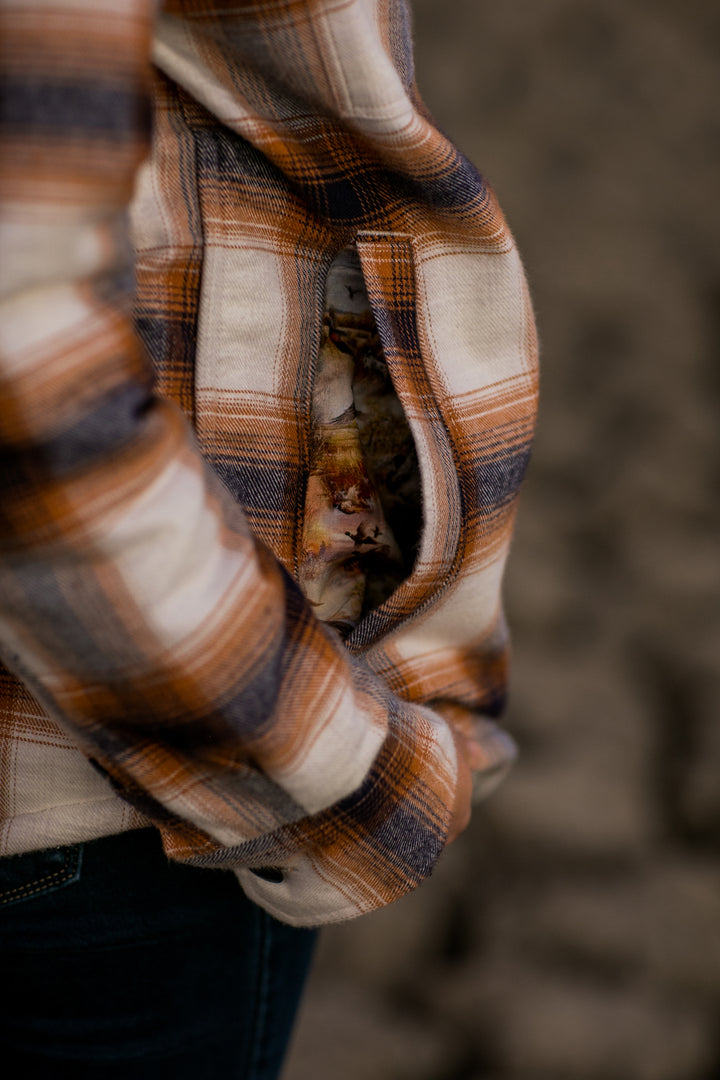 Woman in a Pladra Northwood Sherpa Insulated Flannel Jacket—Peak White, hand in pocket, holding an onion.