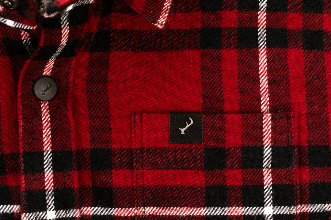 Close-up of the Toddler Cubs Flannel Shirt- Rocky Red, a premium cotton toddler shirt in red, black, and white plaid with black buttons and a small black tag featuring a white antler logo above the front pocket.