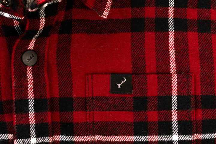 Close-up of the Toddler Cubs Flannel Shirt- Rocky Red, a premium cotton toddler shirt in red, black, and white plaid with black buttons and a small black tag featuring a white antler logo above the front pocket.