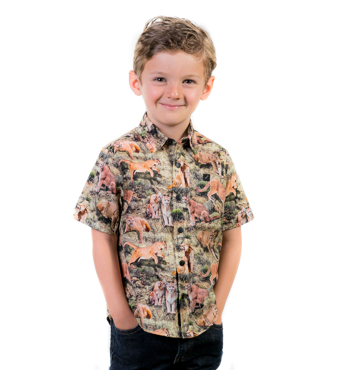 Smiling boy wears Pladra Toddler Cubs Outdoor Aloha Shirt – Mountain Lions, hands in pockets, on white background.
