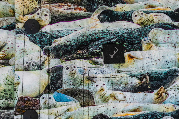 A close-up of the 100% cotton Toddler Cubs Outdoor Aloha Shirt- Seals shows a vibrant print of multiple seals, black buttons, and a small black tag with a white antler logo.