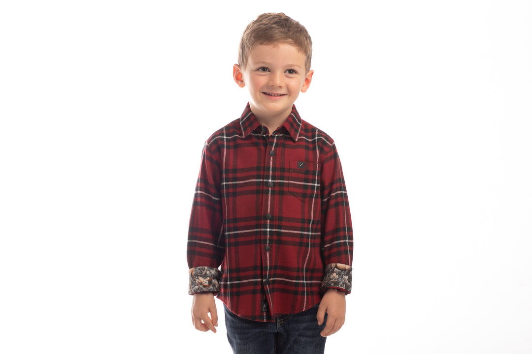 A young boy with light brown hair smiles in the Toddler Cubs Flannel Shirt- Rocky Red, featuring rolled-up sleeves, paired with dark jeans against a white background. Premium cotton flannel provides comfort and style for any occasion.