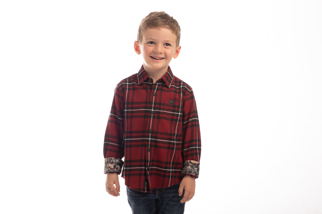 A young boy with short light brown hair smiles against a white background, wearing the Toddler Cubs Flannel Shirt- Rocky Red with rolled-up sleeves and dark jeans.