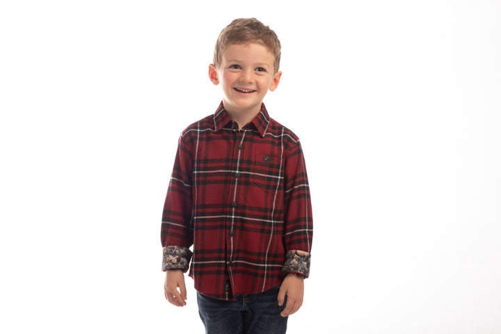 A young boy with short light brown hair smiles against a white background, wearing the Toddler Cubs Flannel Shirt- Rocky Red with rolled-up sleeves and dark jeans.
