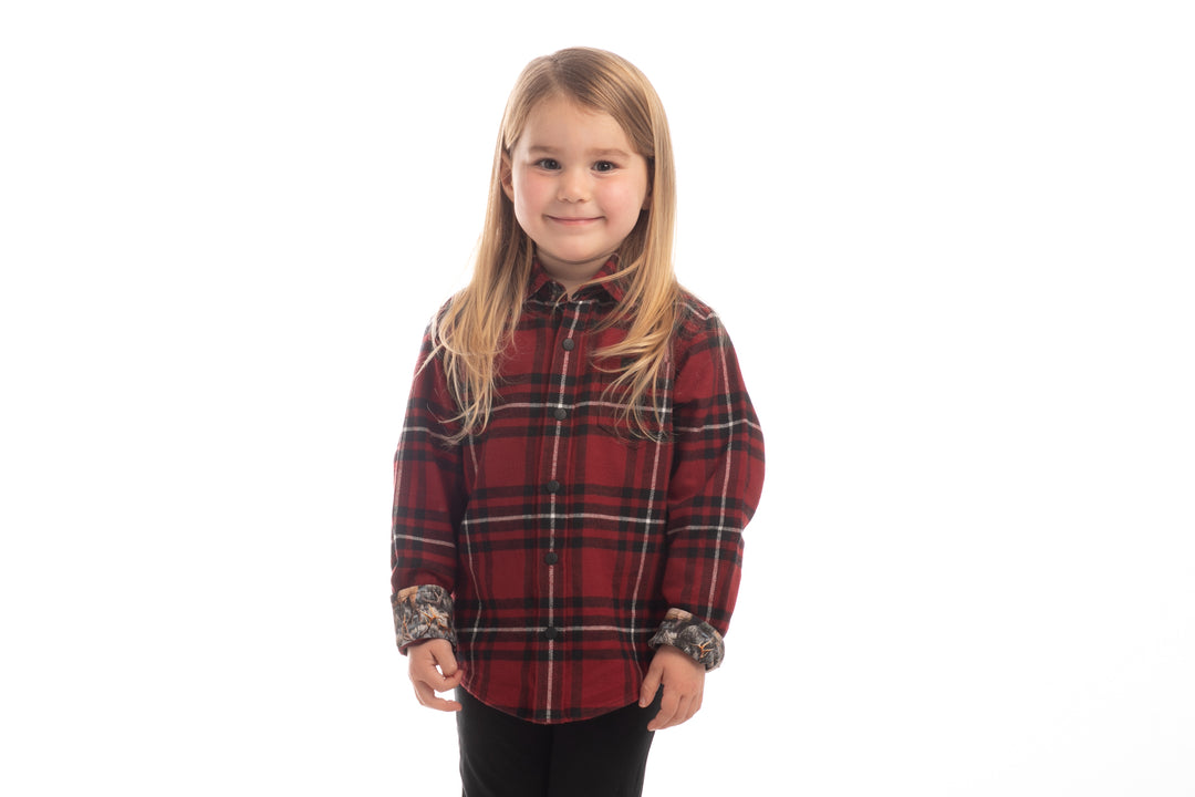 A young girl with long blonde hair, wearing the Toddler Cubs Flannel Shirt- Rocky Red and black pants, stands against a white background and smiles at the camera.