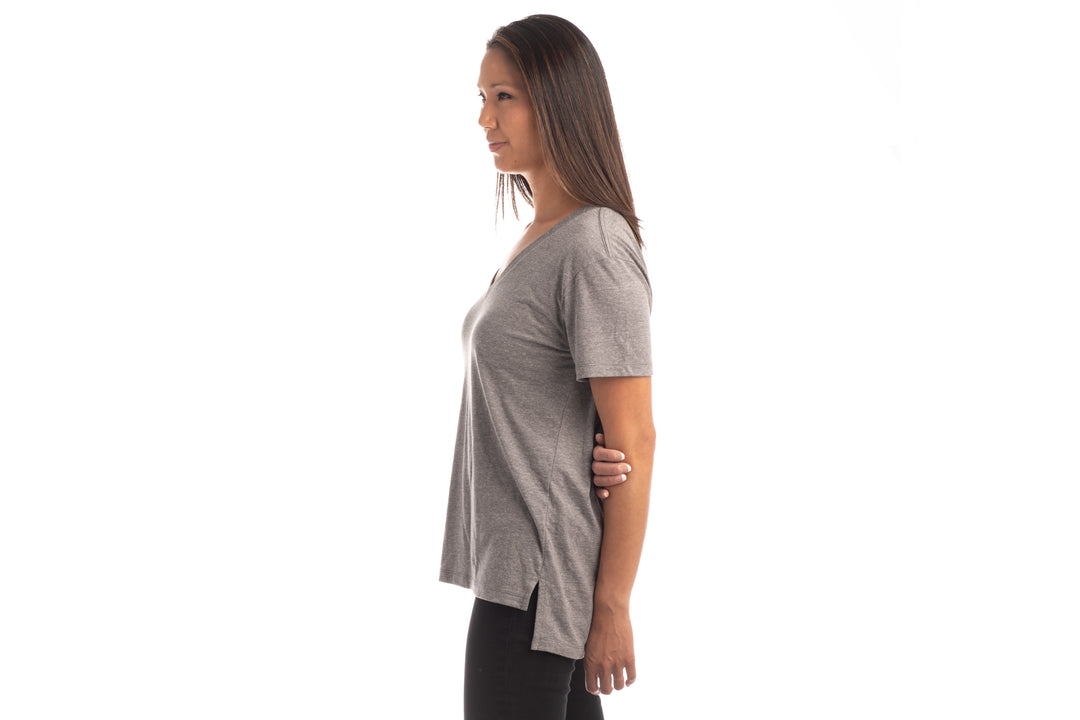 A woman with straight brown hair stands in profile against a white background, wearing a Women&